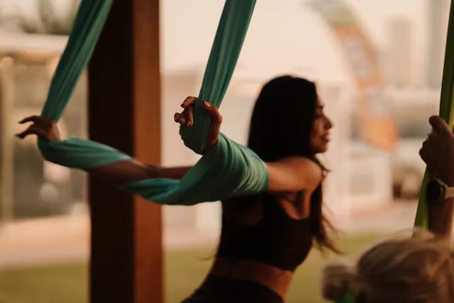A woman smiles as she grips teal aerial silks.