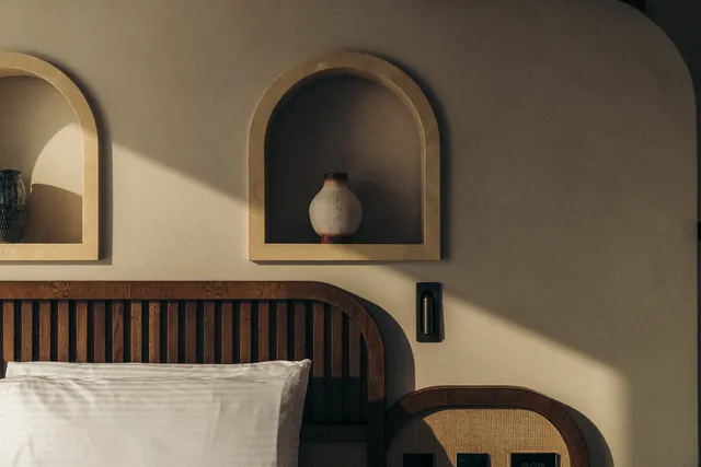 Arched niches with ceramics above a timber headboard in a guest room.