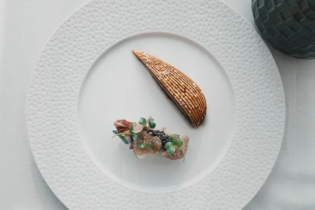 A leaf-shaped chocolate dessert on a textured white plate.
