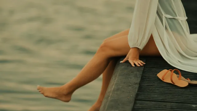 Bare legs over the edge of a timber dock above calm water.