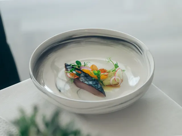 A fish course with citrus, radish and micro greens in a marbled bowl.