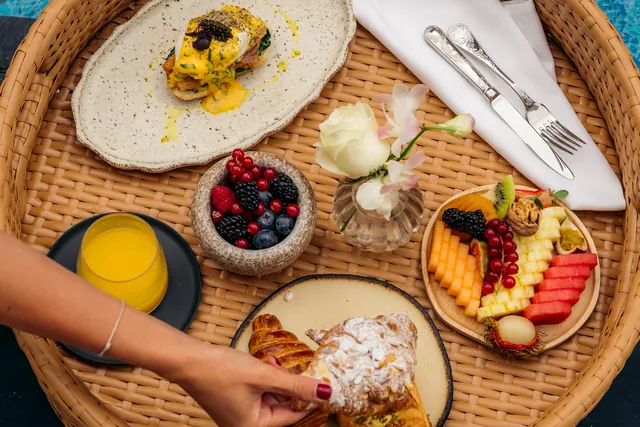 A woven tray of floating breakfast with eggs, berries, tropical fruit and orange juice.