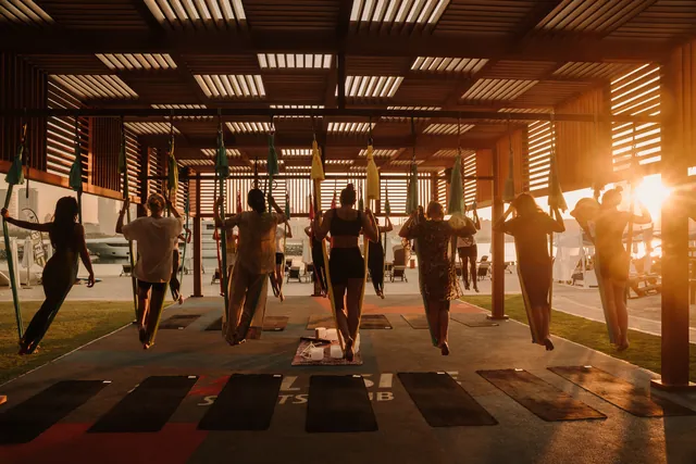 An aerial yoga class under a timber pavilion at sunset.