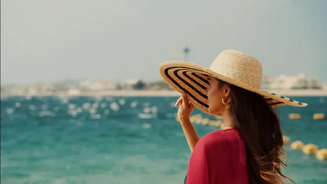 A woman in a straw hat and red top looks out to sea.