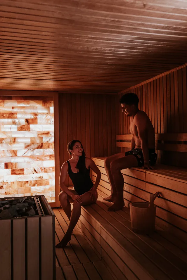 A couple relax in a timber sauna lit by a salt wall.