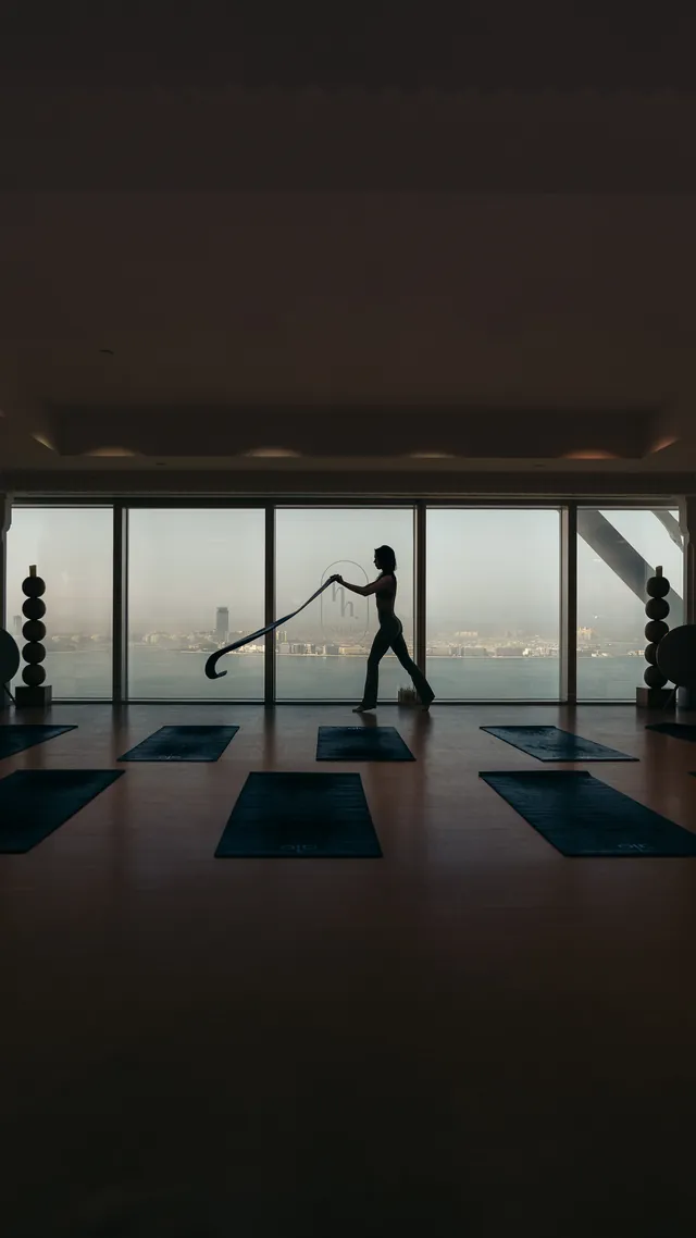A yoga teacher silhouetted against floor-to-ceiling windows above the water.
